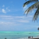 Palme und reetgedeckte Hütte am türkisfarbenen Strand von Jambiani auf Sansibar, im Wasser Boote und Spaziergänger