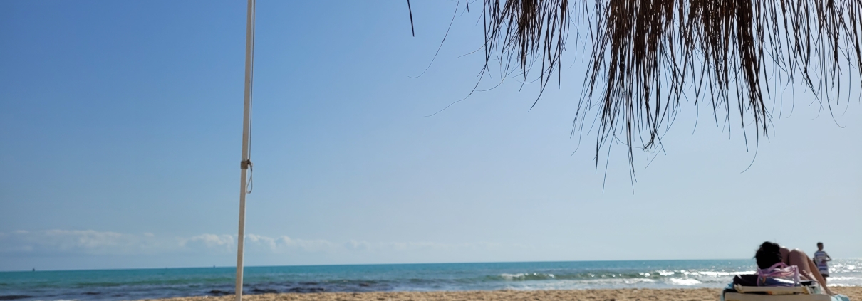 Sandstrand von Hammamet in Tunesien mit reetgedecktem Sonnenschirm und Liegestuhl am Meer